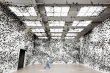 An installation view of a gallery space where the white walls are covered in black paper butterflies.