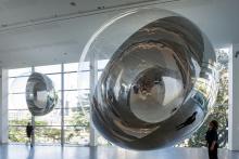 An installation view of enormous silver spheres suspended from the ceiling in a gallery space.