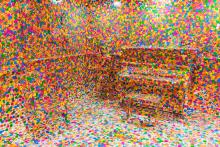An installation view of a room with a piano, but every surface is covered up with colourful dots.