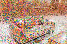 An installation view of a room with a sofa, but every surface is covered up with colourful dots.