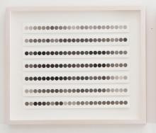 An installation view of an artwork comprised of many dots in varying shades of grey on a sheet of paper, framed in white.