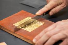 A photograph shows a conservator's hand, poised to cut gold leaf.