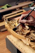 A photograph shows a conservator's hand, performing restoration work on a gilded frame.