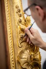 A conservation framer repairs gold gilding on a frame.