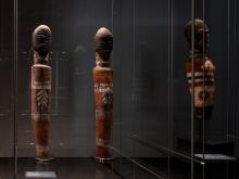 Three figurative carved sculptures installed in a vitrine in a dark gallery space