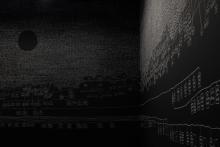 An installation view of a dark gallery space, where the artwork is created in white chalk over the black walls; the centre of the space includes an elevated platform covered in stacks of paper