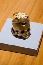 A photograph of a small human skull carved from ivory, with a snake twisting about it in pursuit of a frog.