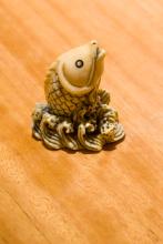 A photograph of a tiny, 5cm-tall fish carved from ivory; it appears to be leaping from frothy waves.