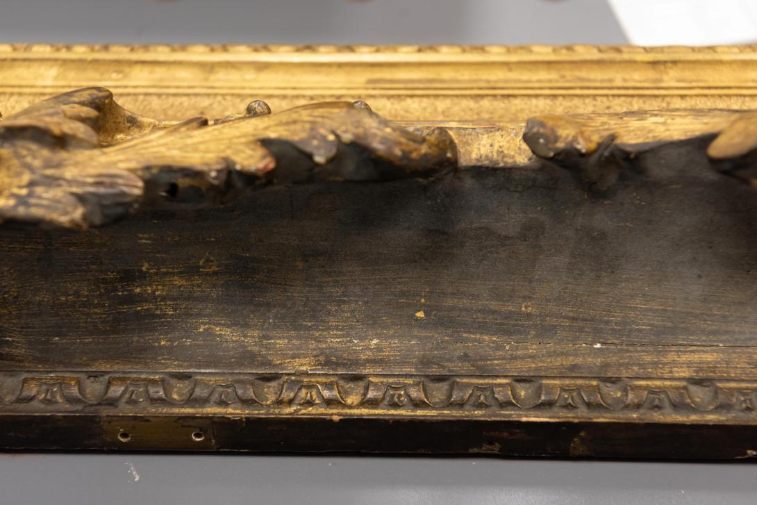 A close-up photo of a section of gilded frame darkened by historical dirt and dust.