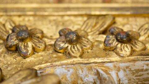 A close-up photograph of three gold-gilded flowers carved into a pine frame from 1771.