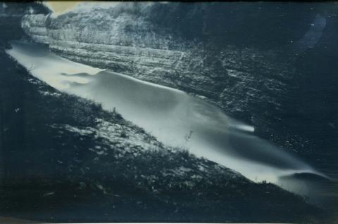 A grey-toned daguerreotype photograph of a river running through a ravine.
