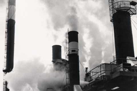 A black-and-white photograph of steam rising from towers at a factory.
