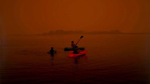 A photograph of someone kayaking under a red post-bushfire sky.