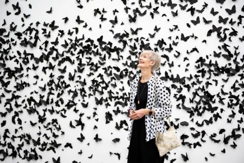 An installation view of a gallery space where the white walls are covered in black paper butterflies.