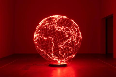 An installation view of a sculpture taking the form of a globe, with the borders of countries lit up in red.