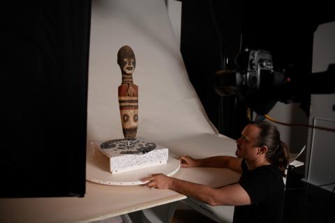 A small wooden figure being set up in a studio by a photographer.