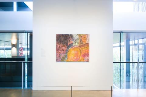 Tommy Mitchell’s Walu Rockhole Dreaming, Emu Heart, The Boy Who Turned Into Wind 2012, installed for ‘Journey’, GOMA, September 2023 / © Tommy Mitchell/Copyright Agency / Photograph: C Callistemon, QAGOMA / A colourful painting installed on a gallery wall, with windows either side.