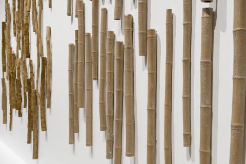 A detail view of a sculptural work installed on a wall, taking the form of many bamboo branches made from clay.