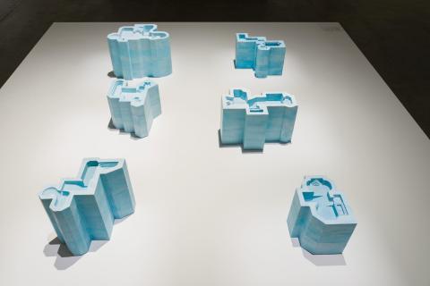 An installation view of six sculptures in the shape of swimming pools, cast in blue-painted plaster.