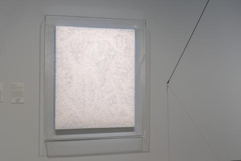 A photograph of a pale-coloured painting installed on a blue wall in a gallery space