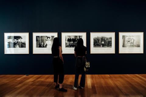 Black-and-white photographs installed on a dark gallery wall, with two people looking on
