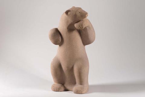 A sandstone sculpture of a bear standing up and looking over its shoulder