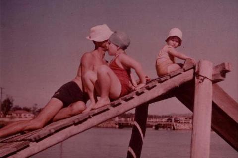 A faded-tone photo of a young family on a pier over water, dressed in swimsuits