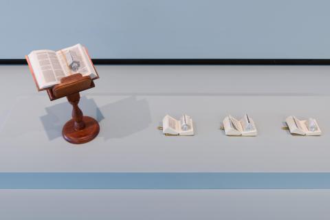 Four sculptural works resembling tiny books, with the pages shaped into even tinier three-dimensional church shapes, installed in a gallery vitrine