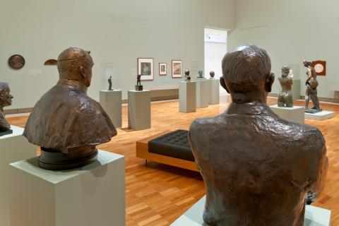 Bronze statues installed on plinths in a gallery space with sage green walls