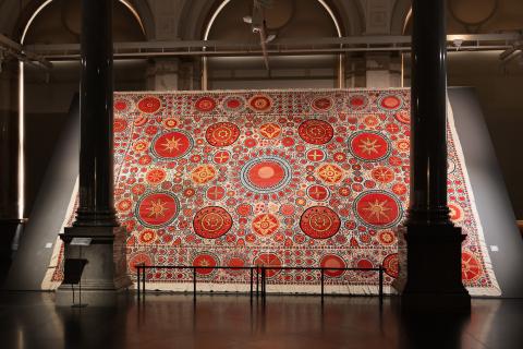 A large, red-patterned textile work installed in a gallery space with grand architectural pillars