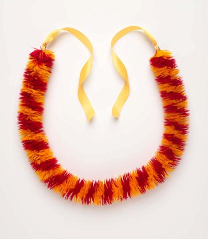 A lei made from orange and red feathers and yellow ribbon, photographed on a bright white background