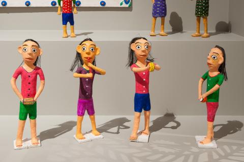 A view of small sculptures of human figures dressed in brightly coloured clothes, installed in a dynamic gathering 