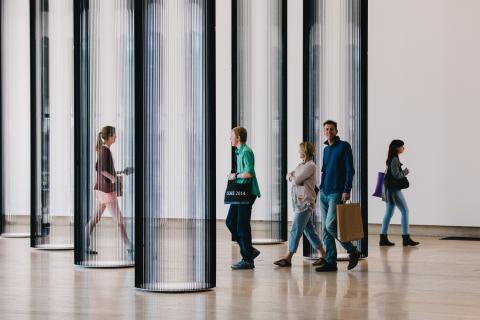 A view of gallery visitors walking through an installation that takes the form of transparent black columns, which are made of the tape from inside video casettes.