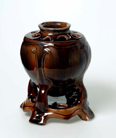 Artwork Vase on stand this artwork made of Earthenware, hand-built oviform with four legs and platform base. Holes pierced around neck, carved and with brown glaze, created in 1932-01-01