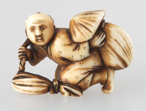 Artwork Netsuke:  (crouching man with a bundle) this artwork made of Carved ivory, created in 1800-01-01