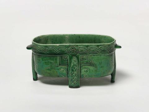 Artwork Footed bowl this artwork made of Hand- and slab-built white earthenware clay set on four feet (at the centres) and lug handles.  Incised rope decoration around the rim with scale pattern on  the legs.  Green glaze, created in 1922-01-01