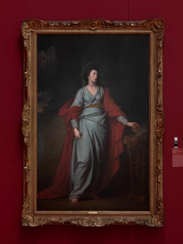 An oil painting of a woman in a blue dress and red robe, with an ornate gold frame, hung on a dark red wall.