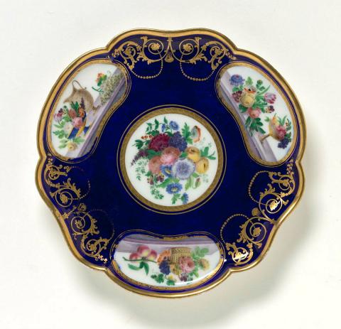 Artwork Footed plate this artwork made of Soft-paste porcelain, lobed trefoil shape in bleu roi ground reserving a central circular shape and three kidney shapes painted with floral bunches.  Gilt scrolls, created in 1764-01-01