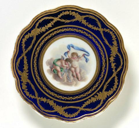Artwork Lobed footed plate this artwork made of Soft-paste porcelain painted with a pair of cupids in a circular reserve against a bleu roi border with gilt, interlacing foliate and floral bands, created in 1800-01-01