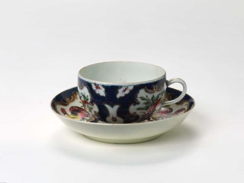 Artwork Cup and saucer:  (dishevelled birds) this artwork made of Soft-paste porcelain, with deep blue scale ground, reserved cartouches decorated with exotic birds and insects in overglaze colour.  Gilt scrolls, created in 1770-01-01