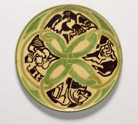 Artwork (Platter with Celtic tracery and stylised zoomorphic figures representing the four apocalyptic beasts) this artwork made of Terracotta clay, wheelthrown, with green, cream and brown-black glazes, incised, created in 1948-01-01