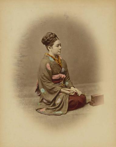Artwork (Kneeling woman with pipe and tobacco box) (from 'Japan' album) this artwork made of Hand-coloured albumen photograph on board (originally bound in an album), created in 1870-01-01