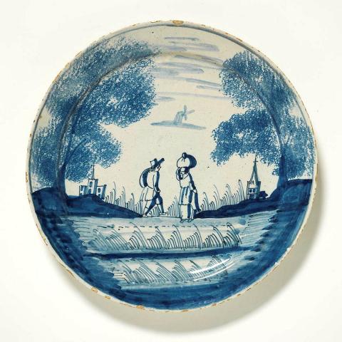 Artwork Plate, decorated with blue and white design showing two figures walking in a European landscape with buildings, church and windmill this artwork made of Earthenware, wheelthrown and tin glazed with cobalt decoration, created in 1700-01-01