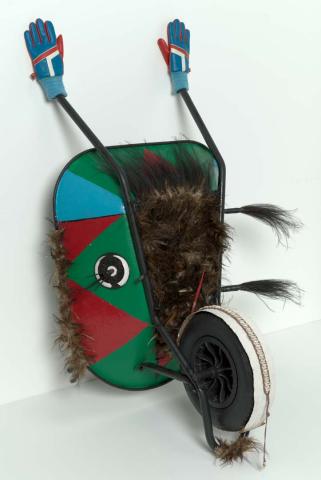Artwork Awari (flying fox) this artwork made of Steel wheelbarrow, synthetic polymer paint, timber spearheads, cassowary feathers, woven natural fibre, braided cord, cowrie shells, vinyl gloves