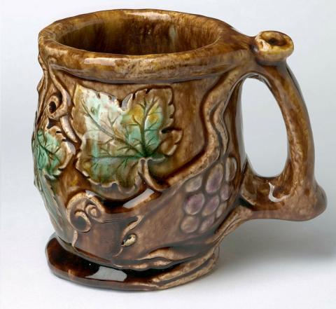 Artwork Wine mug: David this artwork made of Earthenware, modelled with grape leaf, fruit and tendrils, the branch forming the handle. Glazed mulberry and green over brown, created in 1937-01-01