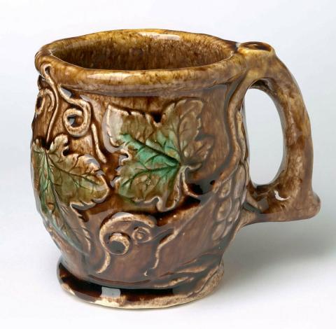 Artwork Wine mug: Bruce this artwork made of Earthenware, modelled with grape leaf, fruit and tendrils, the branch forming the handle. Glazed mulberry and green over brown, created in 1937-01-01