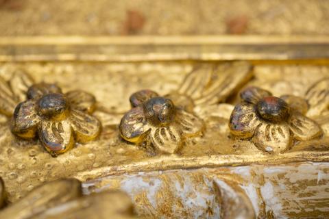 A close-up photograph of three gold-gilded flowers carved into a pine frame from 1771.