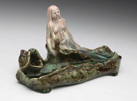 Artwork Pen tray this artwork made of Earthenware, modelled with a reclining mermaid and a dolphin grotesque, the irregular rectangular base in mixed clay with green glaze, created in 1920-01-01