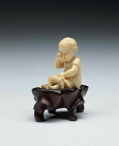 Artwork Figurine this artwork made of Ivory, carved in the form of a seated child and wooden stand, created in 1800-01-01