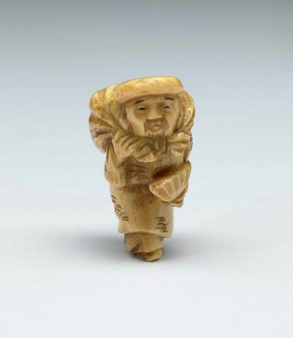 Artwork Netsuke:  (man carrying fan and pack) this artwork made of Ivory, carved and incised, created in 1800-01-01